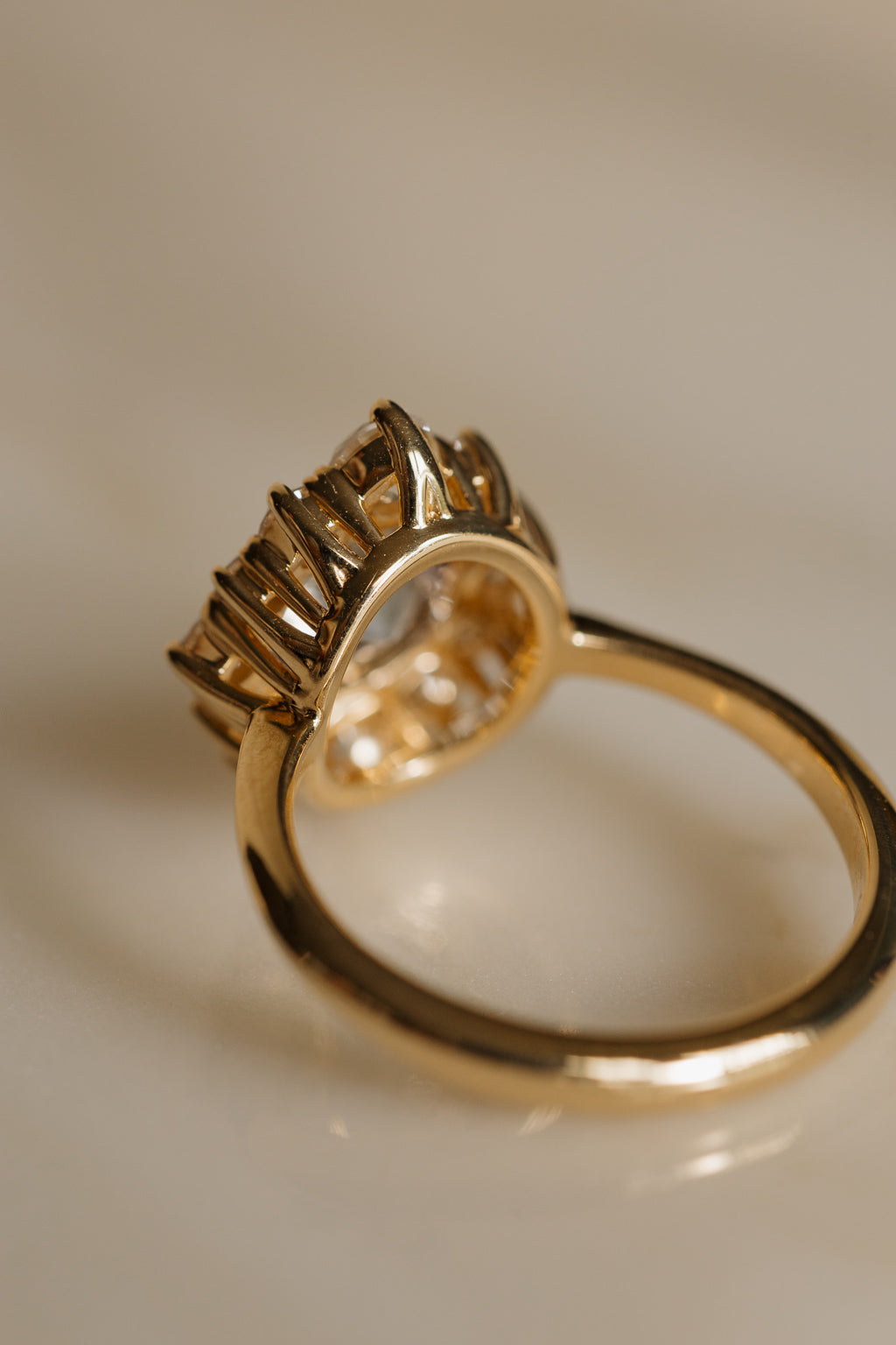 View from behind a yellow gold engagement ring showing the open gallery beneath the halo, with tall claw prongs rising around the stones and a smooth, rounded band.