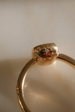 Close view of the side and underside of a yellow gold engagement ring's bezel cup, showing a star-set diamond between two engraved stars, the milgrain edge of the band, and a grooved band detail, on a reflective cream marble surface in warm light.
