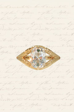 An engagement ring with a yellow gold old-world wheat hand-engraved band, a split shank, and four claw prongs in a compass setting around an old mine cut diamond.
