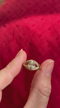 Video featuring an engagement ring turning in the sunlight between two fingers. The ring is yellow gold with an old-world hand engraved split shank band. The center stone is an old mine cut diamond with four claw prongs in a compass setting. The split shank has a hidden halo made of emeralds on the lower profile of the side view. 