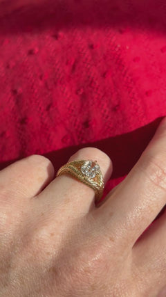 Video of a hand wearing an old mine cut diamond engagement ring. The ring is yellow gold and has an old-world wheat engraved split shank band. There are four compass set prongs on the edges of the center stone.