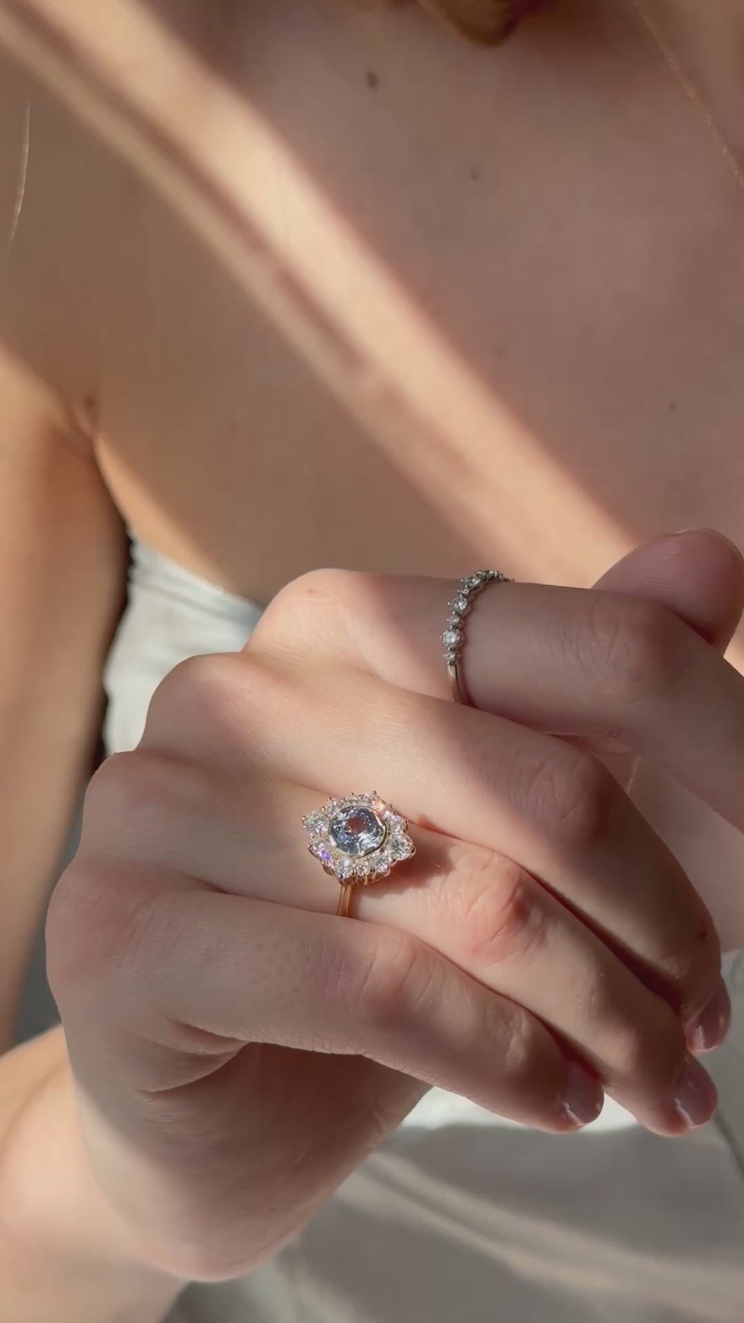 Close-up video of a hand wearing a pale blue sapphire halo engagement ring, moving slowly through a narrow streak of sunlight as the diamonds catch the light.