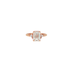 Close-up of a three stone engagement ring featuring an emerald cut diamond with triangle cut accent diamonds, set in rose gold with a hand-engraved band and milgrain detail.