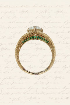 Side view of a Moonryvr engagement ring with a yellow gold, old-world, hand engraved, split shank band. The center stone is an old mine cut diamond with four claw prongs in a compass setting. The split shank has a hidden halo made of emeralds on the lower profile of the side view. 